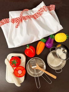 Kids kitchen play set with apron, toy vegetables and mini cooking utensils on wood
