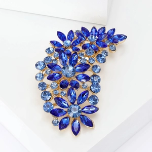Vintage floral alloy brooch with blue crystals on gold base in bright studio setting