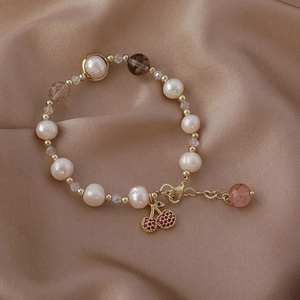 Detail of baroque pearl bracelet with red cherry pendant on elegant silk background