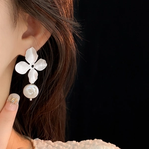 Close-up of silver metal flower earrings with white pearl pendant worn by a model