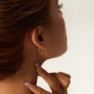 Elegant gold heart-shaped stainless steel hoop earrings worn for a minimalist fashion look