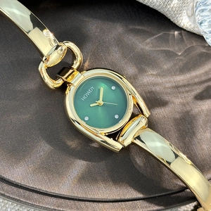 Detail of horseshoe case women watch with green dial and gold bangle bracelet