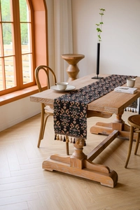 Floral jacquard table runner with decorative tassels on a rustic wooden dining table
