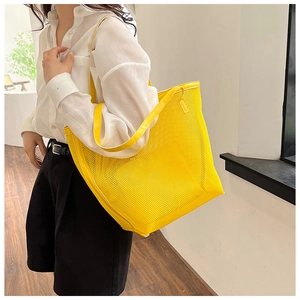Detailed view of large yellow mesh beach tote bag worn by a model on shoulder