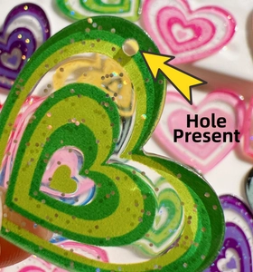 Close-up of glittery heart-shaped resin beads with pre-drilled holes for DIY jewelry