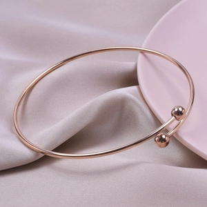 Close-up of rose gold stainless steel open bangle with smooth sphere ends on satin fabric