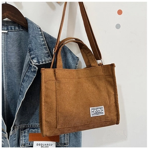 Brown corduroy tote bag with front pocket and adjustable strap hanging on a hanger