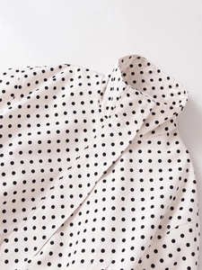 Detalle del cuello alto y el estampado de lunares negros en la chaqueta tejida blanca