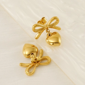 Golden stainless steel earrings with bow design and hanging heart charm on white fabric