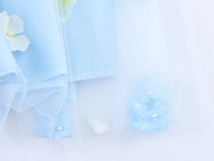 Detail of 3D light blue flower applique with white pearl center on sheer mesh fabric