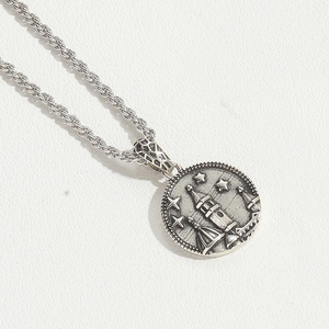 Detail of vintage silver round pendant featuring embossed castle and star on rope chain