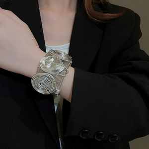 Detailed view of wide woven silver metal spiral cuff bracelet on female wrist