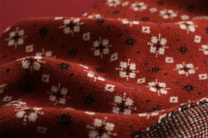 Macro detail of red knitted Christmas scarf fabric with white snowflake pattern texture