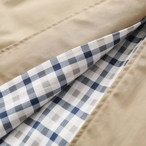 Detail eines khakifarbenen Trenchcoats mit blau-weißem Karofutter und feiner Nahtverarbeitung