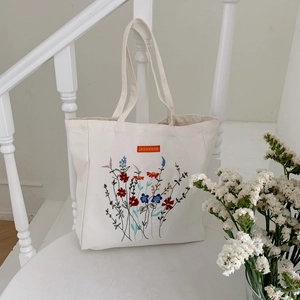 Detail of colorful floral embroidery on a cream canvas tote bag with sturdy straps