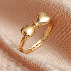 Macro shot of gold bow-shaped adjustable open ring on pink textured silk fabric