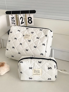 Detail of white quilted toiletry bag set with black bow print and ribbon zippers