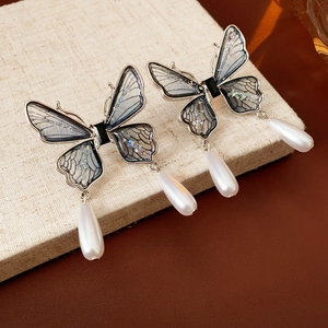 Detailed shot of silver butterfly earrings with grey-blue wings and teardrop pearl drops