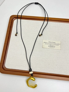 Detail of matte gold C-shaped pendant on black cord with adjustable beads and wooden accents
