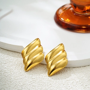 Macro view of 18K gold stainless steel earrings with layered wave textures and polished finish