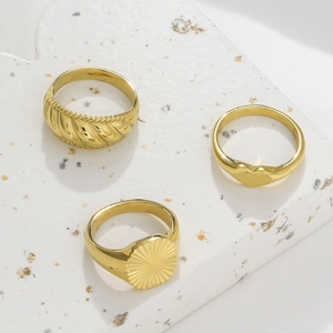 Three gold stainless steel rings featuring braided texture, heart shape, and sunburst seal