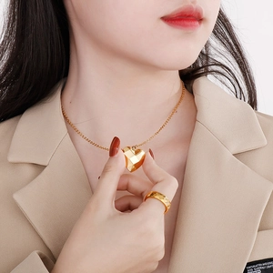 Détail d'un collier doré 18K avec pendentif cœur facetté sur un blazer de couleur beige