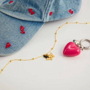 Dettaglio della collana dorata con pendente angelo e perle nere su fondo bianco