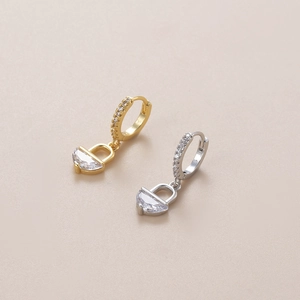 Detail view of gold and silver padlock earrings with zircon-encrusted hoops and charms