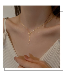 Close-up of golden bow pendant with tassel on a minimalist S925 silver necklace