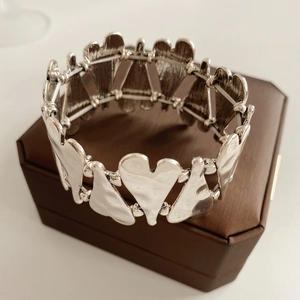 Détail macro du bracelet à maillons cœur argenté avec texture mate sur boîte en cuir