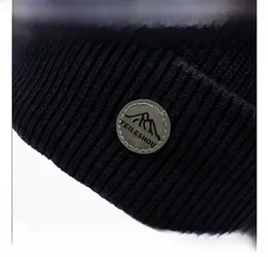 Dettaglio del cappello in maglia a coste con toppa in pelle circolare e logo