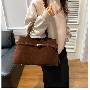 Detail of a brown faux suede tote bag featuring buckle straps and double handles
