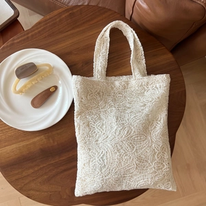 Detail of floral lace embroidery and hollow texture on a cream tote bag handle