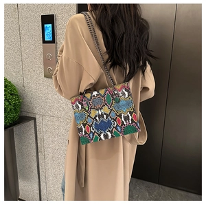 Detail view of colorful snakeskin shoulder bag with gold chain strap on beige trench coat