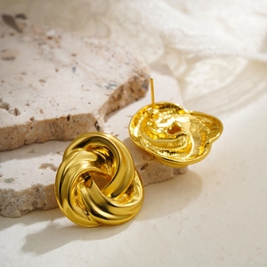 Detail shot of golden twisted knot earrings on stone and lace background, 18K gold plating