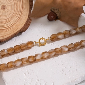 Flat lay of resin beaded necklace with beige and gold glitter square beads on stone