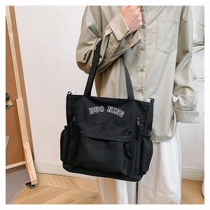 Detail of black canvas tote bag with white letter embroidery worn by a model
