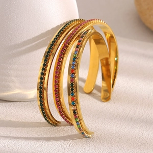Detail of 18K gold-plated stainless steel bangles with colorful zircon inlay on a textured table