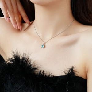 Detail view of a silver square necklace with a blue gemstone pendant on a female model