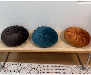 Three plush velvet pumpkin pillows in brown, blue and orange on a wooden bench