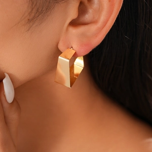Close-up of golden geometric chunky C-shaped earring with polished metallic texture