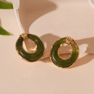 Macro detail of dark green resin earrings with golden metal edges on a beige stone
