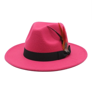 Close-up of rose red wool fedora hat featuring black ribbon and decorative side feathers