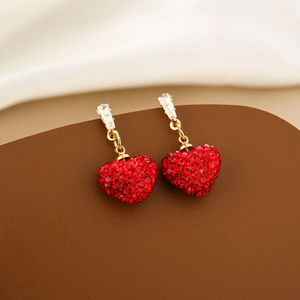 Macro detail of red heart earrings with gold base and faceted crystals on silk