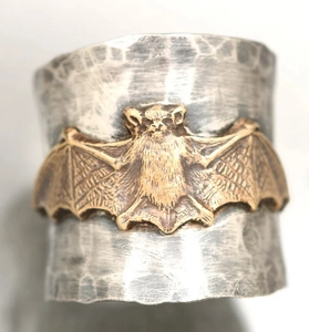 Detailed close-up of wide silver ring featuring a golden bat relief and hammered texture