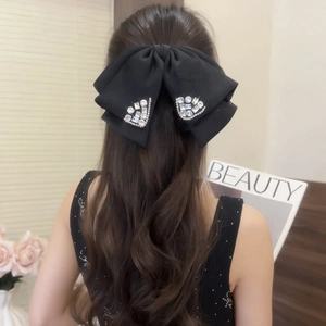Large black fabric bow hair claw clip with rhinestones worn by a model on back of head