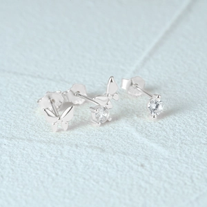 Macro detail of silver butterfly earrings and round cubic zirconia studs on blue surface