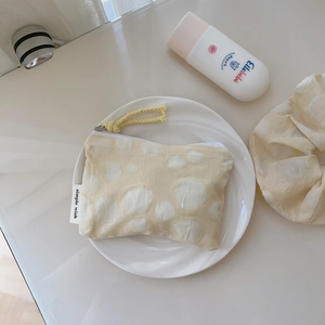 Détail de la pochette en coton beige à pois avec fermeture éclair et étiquette