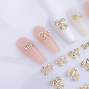 Golden 3D bow nail art charms set with white pearls and sparkling rhinestones