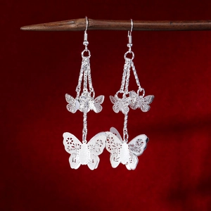 Detailed view of vintage silver butterfly tassel earrings hanging on a dark wood stand